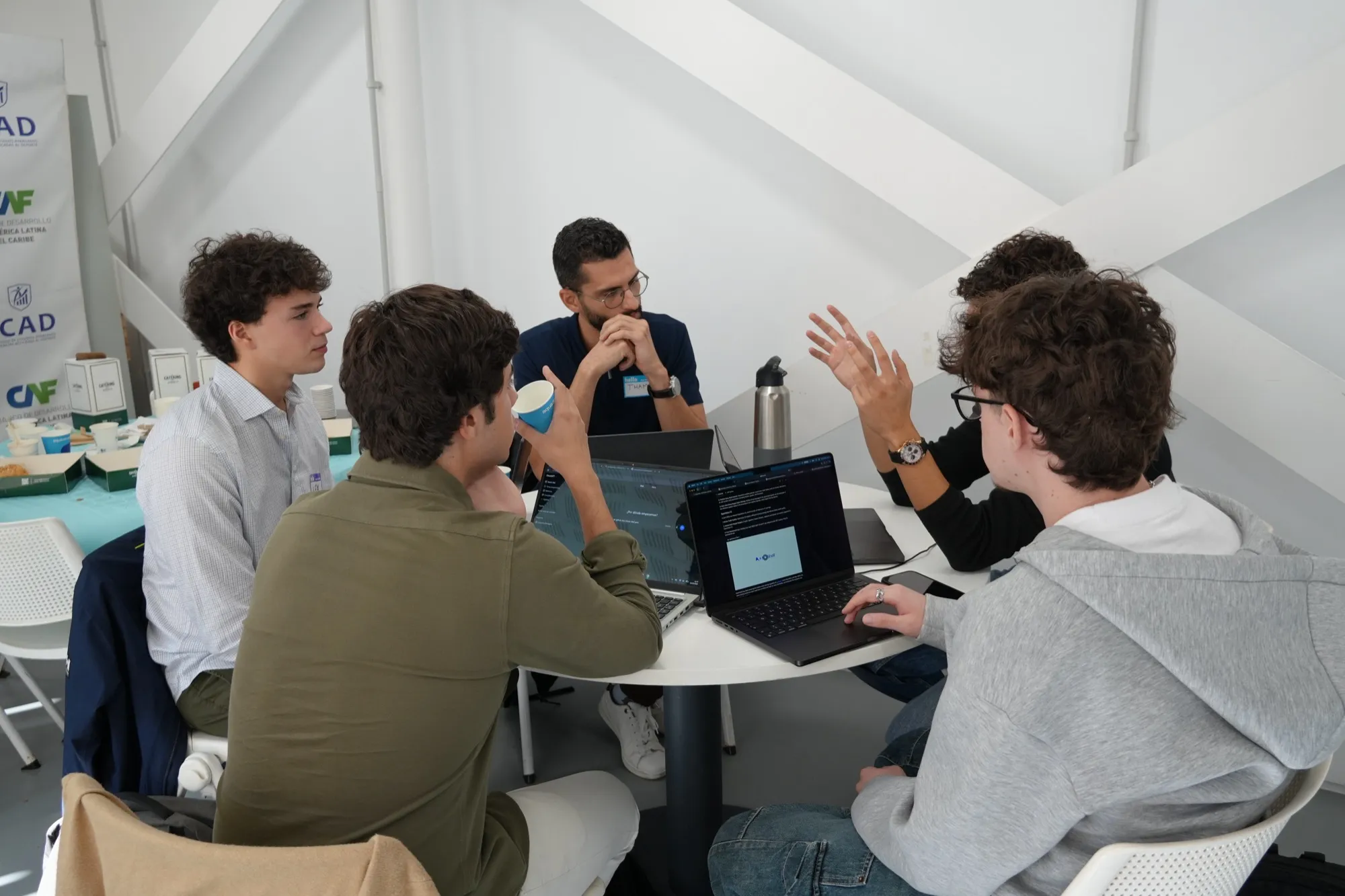 Five people around a round table with laptops, talking